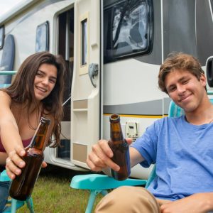 Young couple enjoys a summer vacation with beers at a camper van in Portugal.